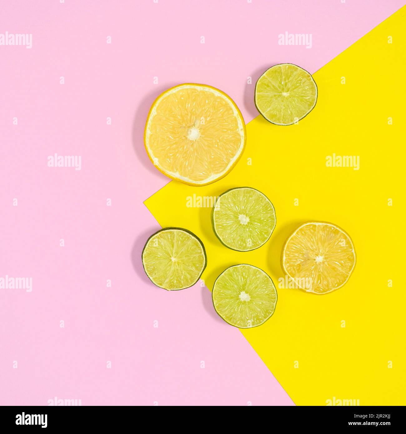 In Scheiben geschnittene Limetten und Zitronen auf pastellrosa und gelbem Hintergrund. Flach liegend Stockfoto