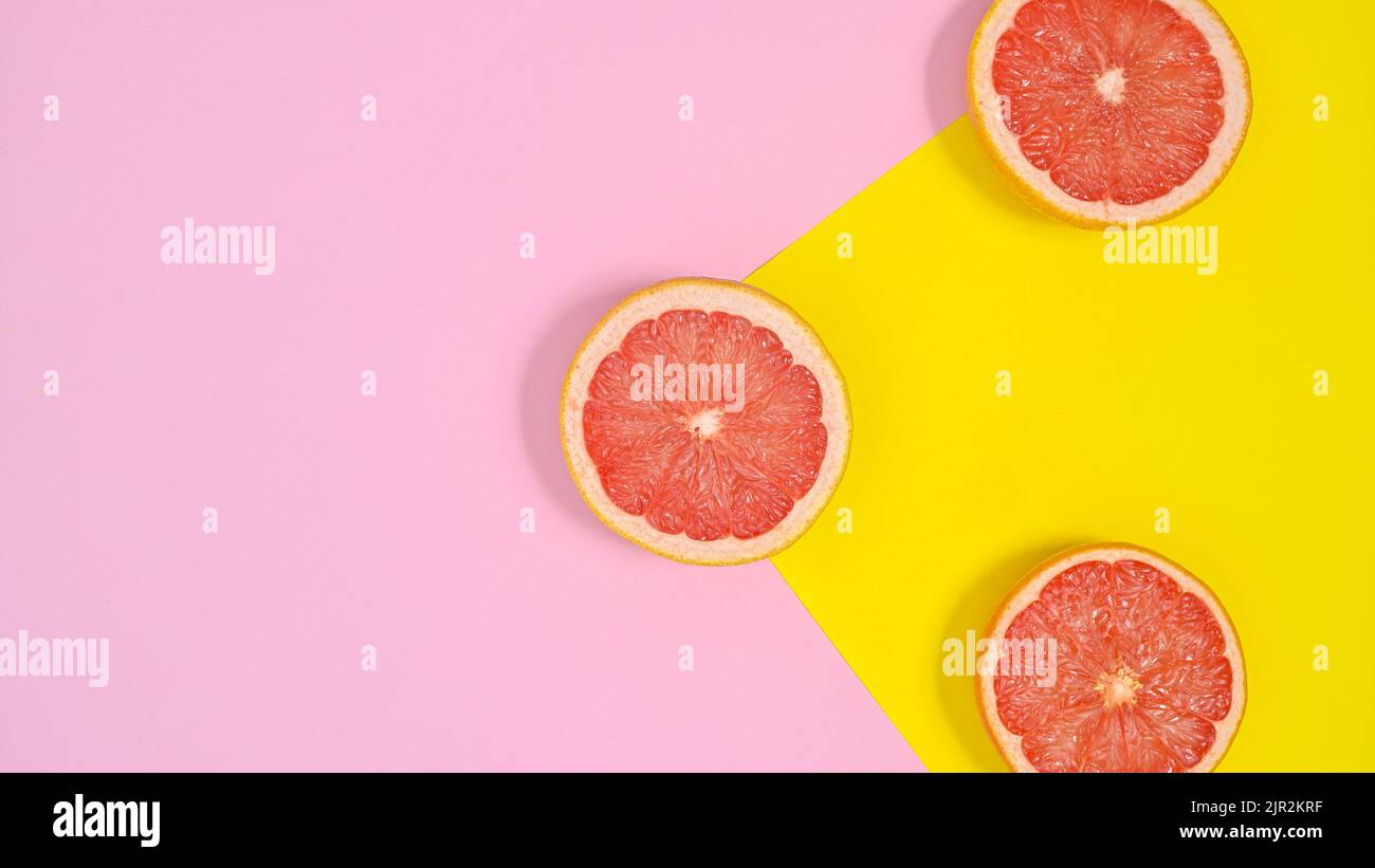 In Scheiben geschnittene rote Grapefruits auf pastellrosa und gelbem Hintergrund. Flach liegend Stockfoto