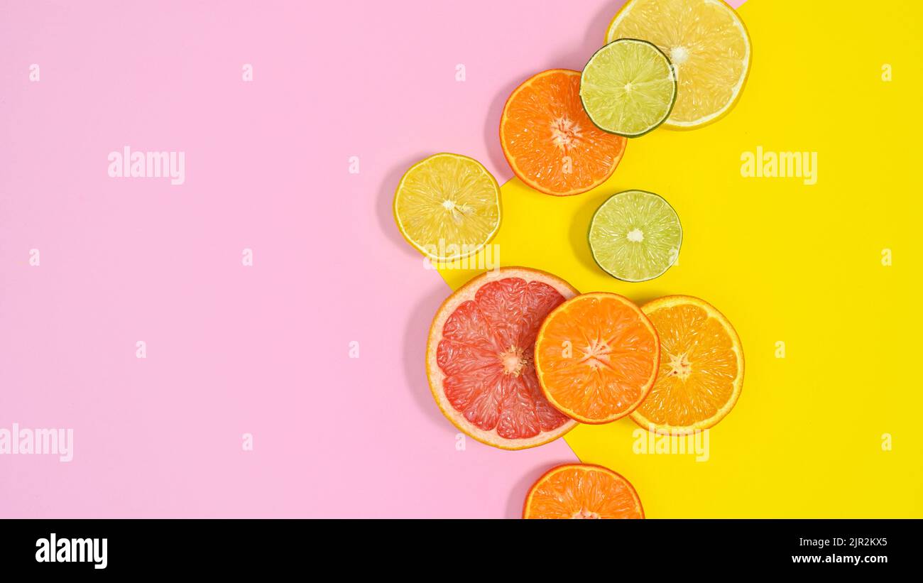 In Scheiben geschnittene Zitrusfrüchte auf pastellrosa und gelbem Hintergrund. Flach liegend Stockfoto