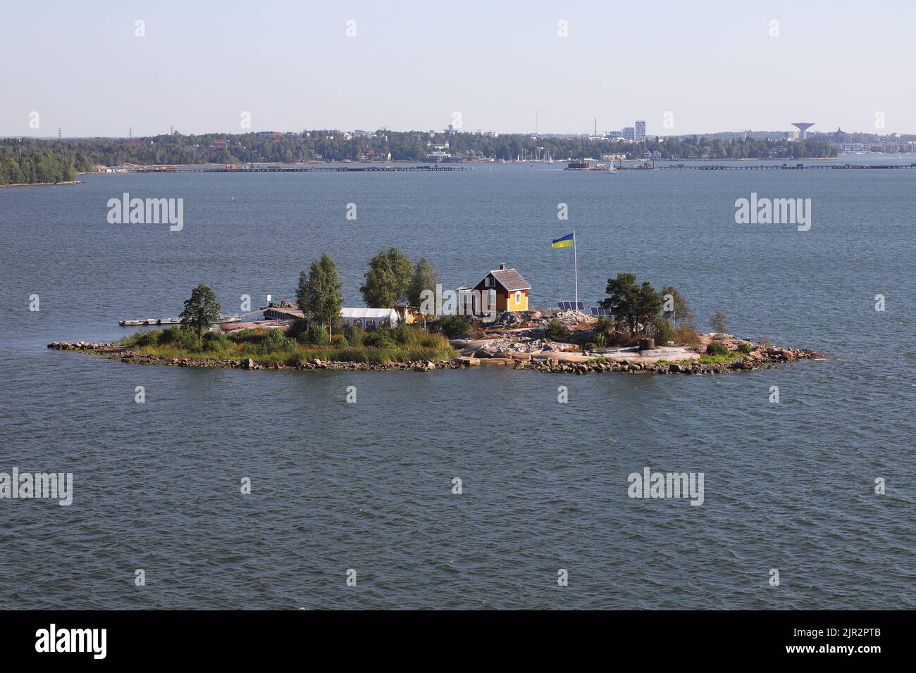 Helsinki, Finnland - 20. August 2022: Die ukrainische Flagge, die neben einem kleinen Haus auf einem kleinen Inselschiff am Eingang des Hafens von Helsinki aufgerichtet ist. Stockfoto