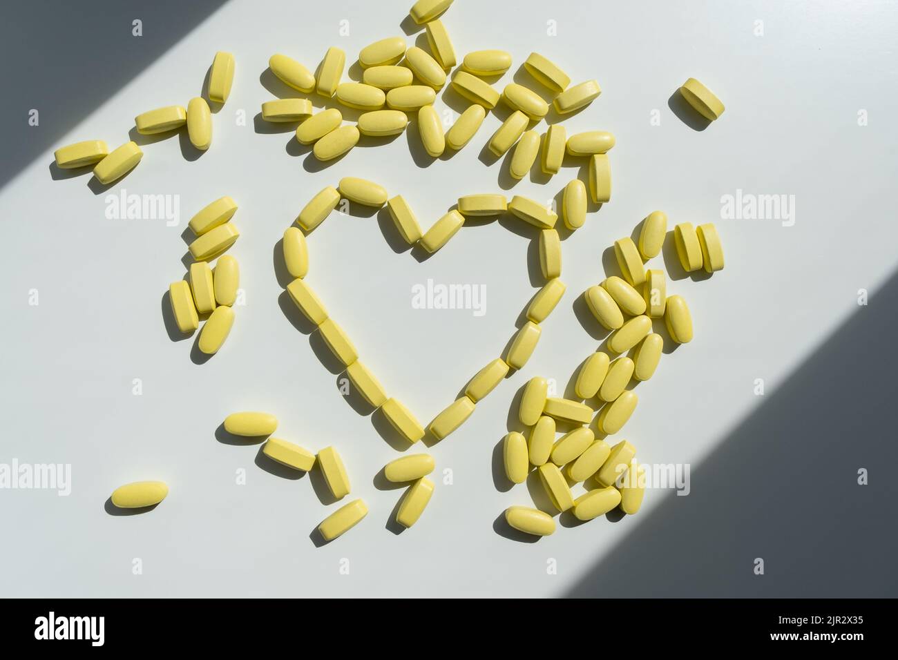 Herz aus gelben Pillen auf weißem Hintergrund. Stockfoto