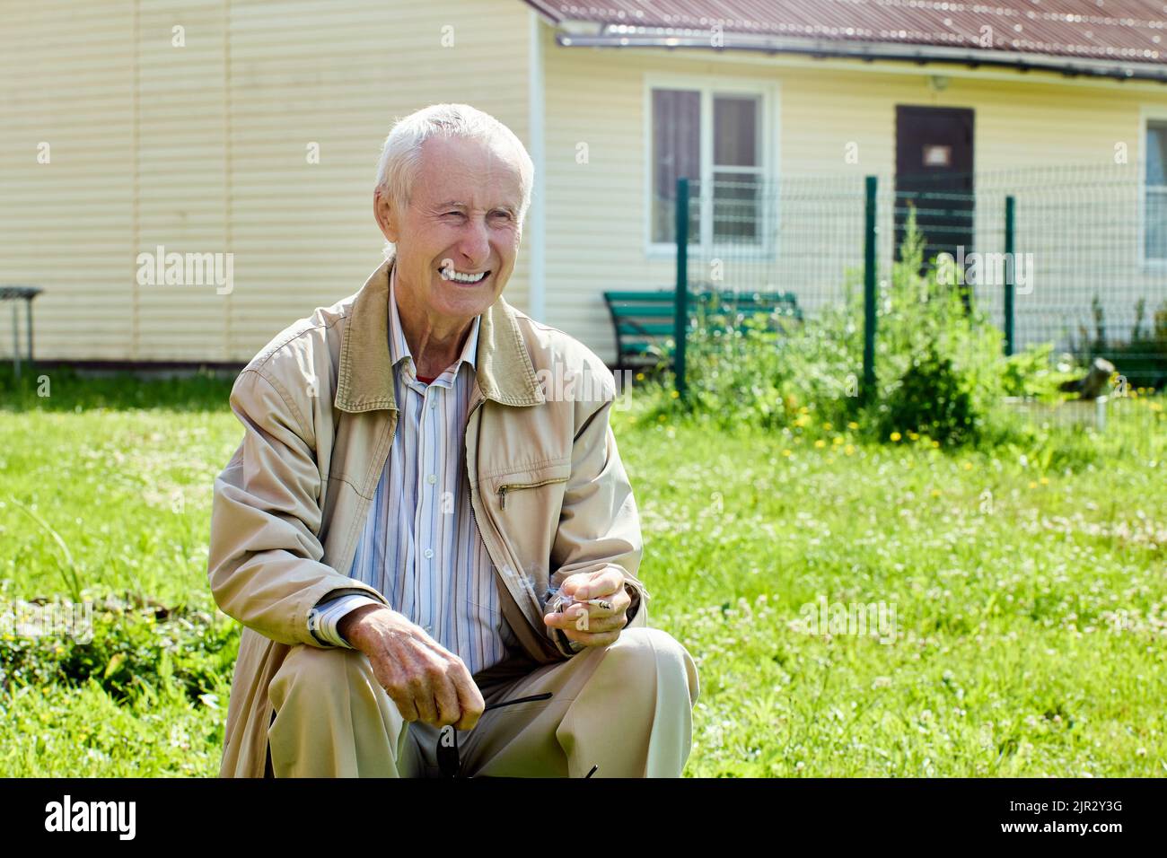 Weiß gezahnt von einem 75 Jahre alten Mann, der draußen vor seinem Haus sitzt. Stockfoto