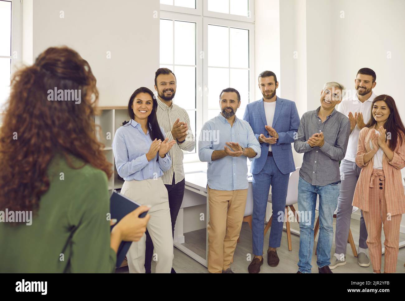 Lächelnde, glückliche Geschäftsleute applaudieren ihrer Kollegin bei der Teambesprechung im Konferenzraum. Stockfoto