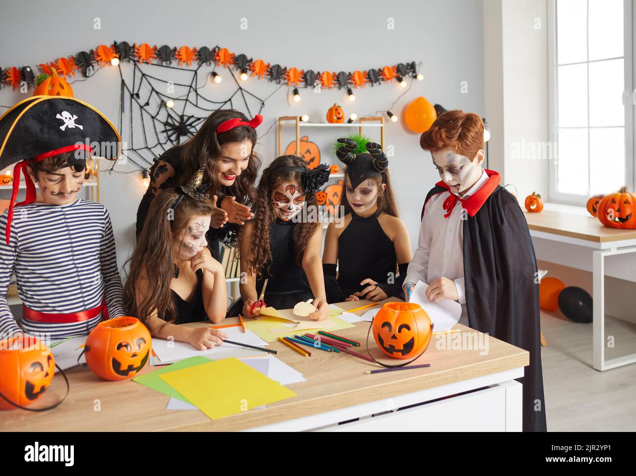 Junge Lehrerin mit ihren jüngeren Schülern schneiden Halloween-Origami im Klassenzimmer aus. Stockfoto