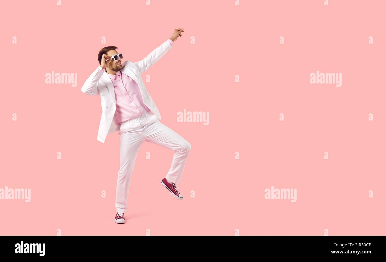 Fröhlicher Partymensch in weißem Anzug und Sonnenbrille, der isoliert auf einem rosa Kopierraum-Hintergrund tanzt Stockfoto