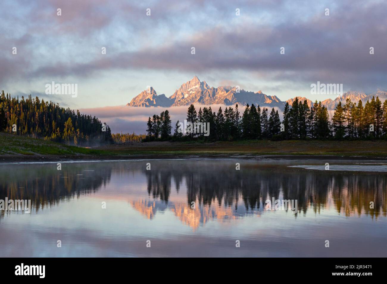 Morning Mists teilen sich, um die Teton Range in all ihrer Pracht zu enthüllen, die sich in stillem Wasser widerspiegelt Stockfoto