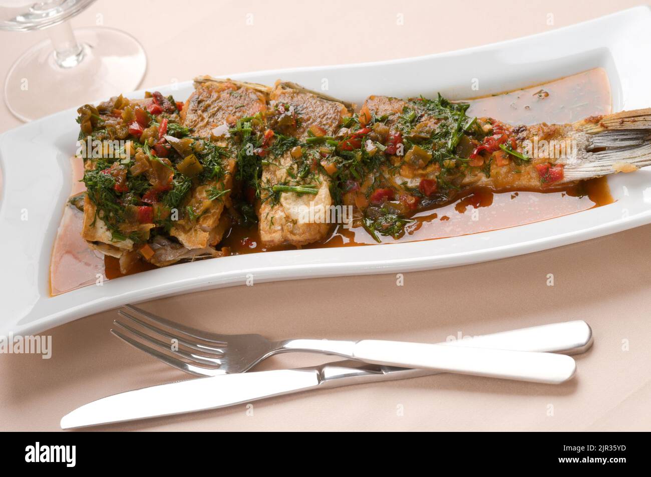 Gerösteter Fisch unter Tomatensauce und Gemüse auf einem langen Teller serviert Stockfoto