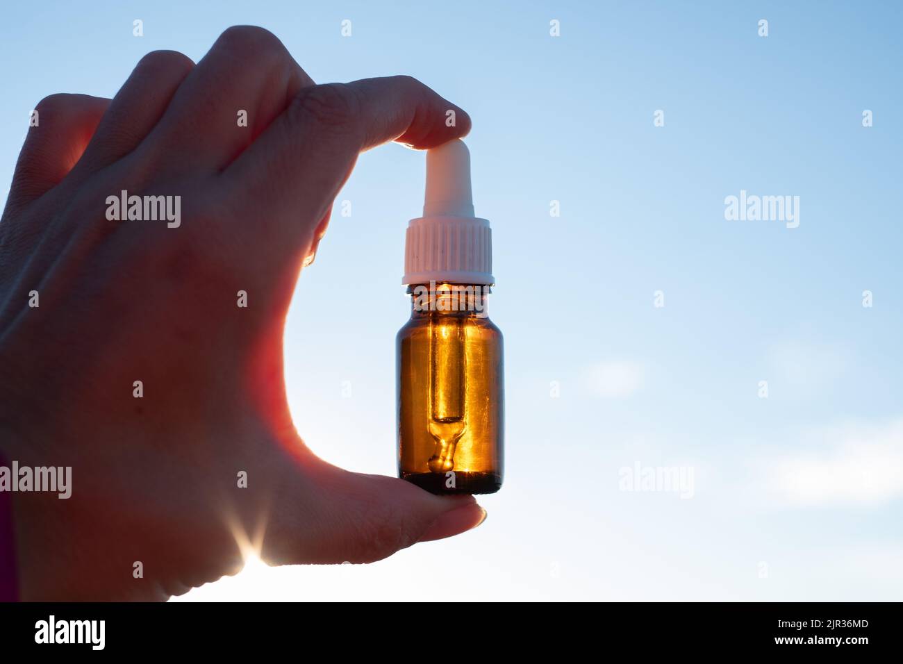 Flasche ätherisches Öl in der Hand gegen sonnigen Himmel. Kleine braune Medizinflasche im Hintergrund der Natur. Hanföl aus biologischem CBD. Stockfoto