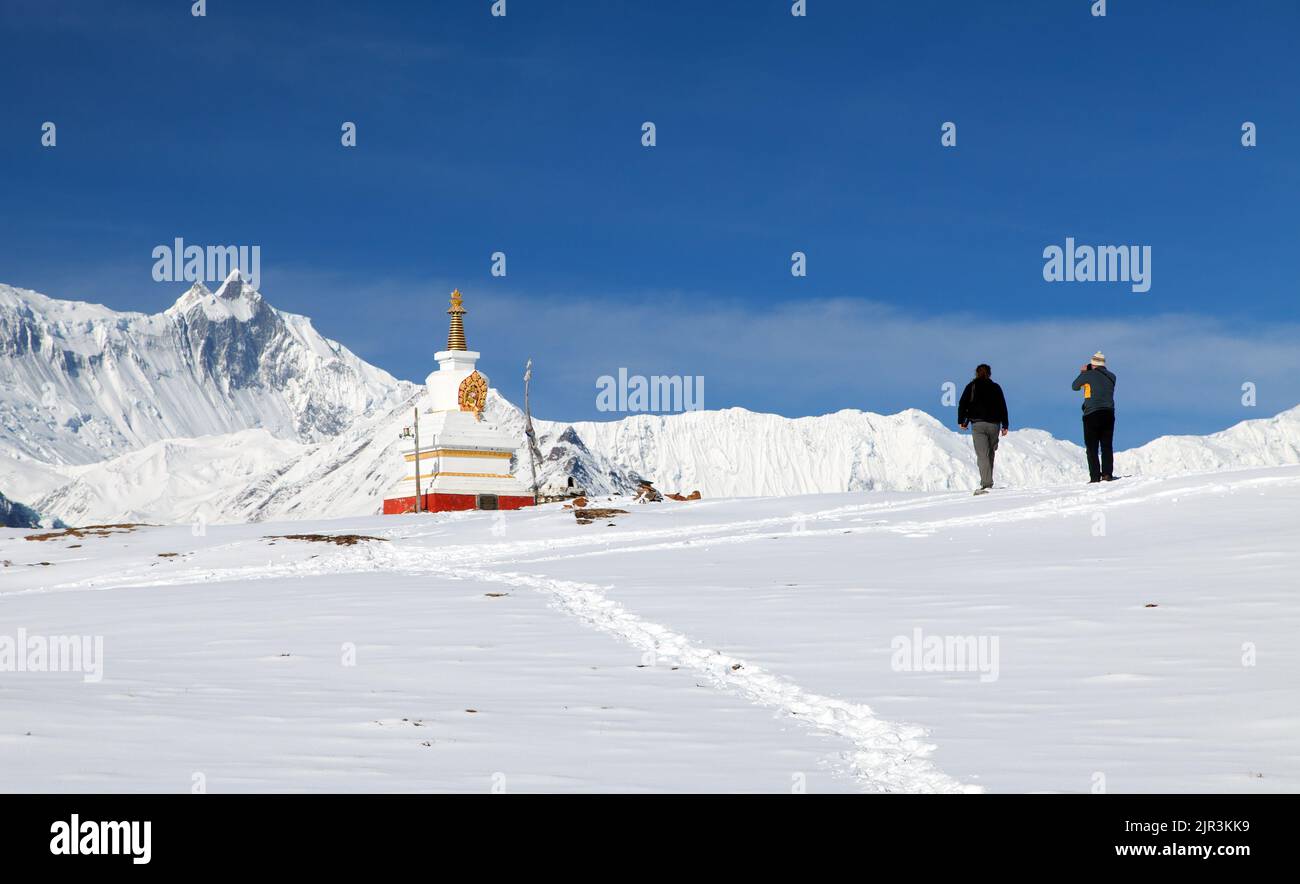 Blick auf die weiße buddhistische Stupa in der Nähe des Eissees (Kicho Tal) und der Annapurna-Reihe mit zwei Touristen, den Berg Gangapurna oder Ganggapurna um die Annapurna-Rennstrecke Stockfoto