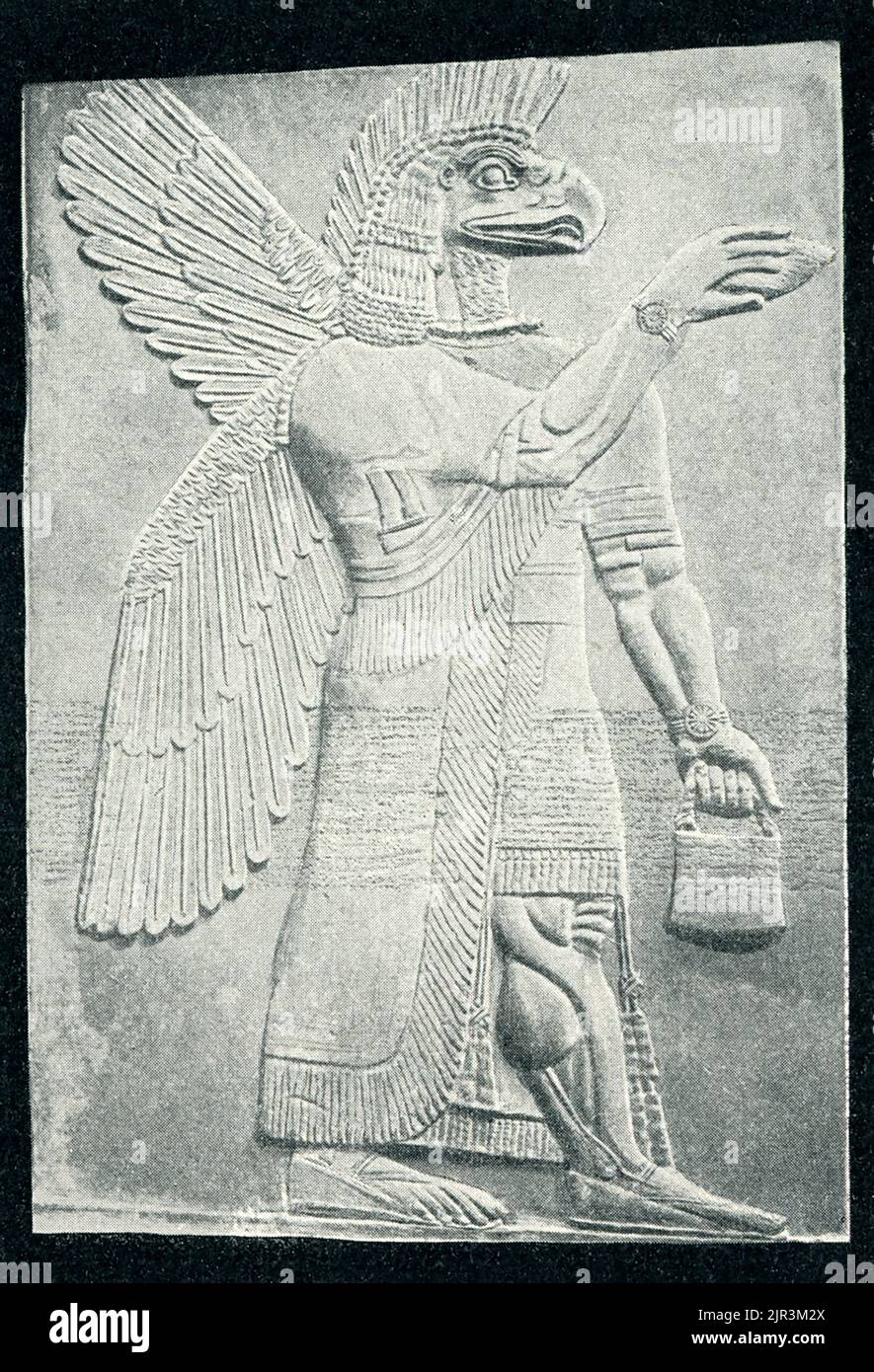 Die 1910 Überschrift lautet: 'Geflügelte Gottheiten - ein assyrisches Relief. Das Original befindet sich im British Museum in London.“ Dieses Genie, oder Demi-gott, war Teil einer Gruppe von geflügelten Kreaturen gegenüber einem stilisierten Baum, eine Szene wiederholt sich zahlreiche Male im Palast. Sie scheinen Fruchtbarkeitsrituale zu machen, die mit der Dattelpalme verbunden sind, einem Baum, der von den Assyrern heilig gehalten wird, weil er Nahrung, Getränke, Holz und Schutz bietet. Dieses Relief, einst hell bemalt, ist ein Fragment aus dem nordwestlichen Palast, der vom assyrischen König Aschirnasirpal II. (883 – 859 v. Chr.) in seiner Hauptstadt Kalhu, der heutigen irakischen Stadt, erbaut wurde Stockfoto