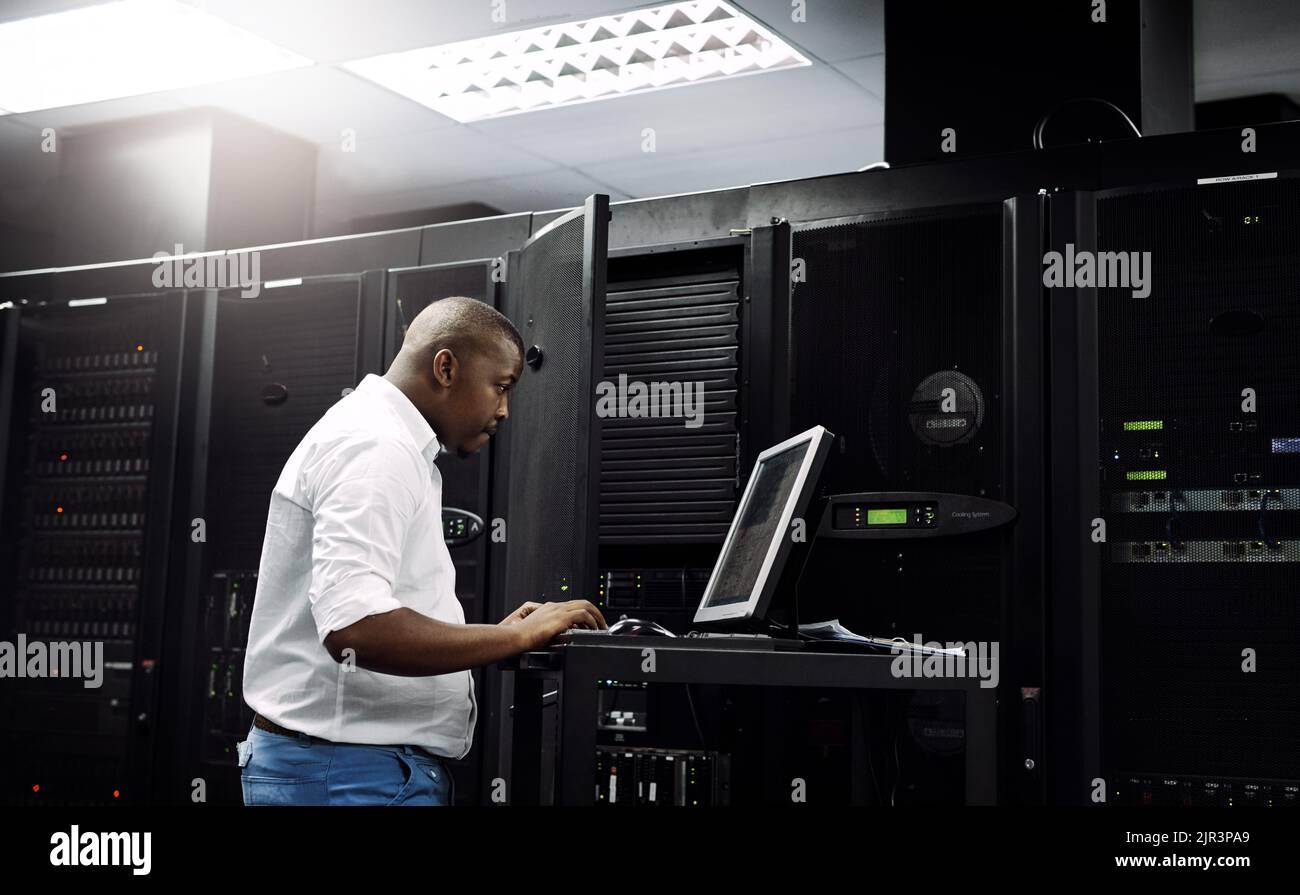 Ein IT-Techniker, der einen Computer verwendet, während er im Serverraum eines Rechenzentrums arbeitet. Stockfoto
