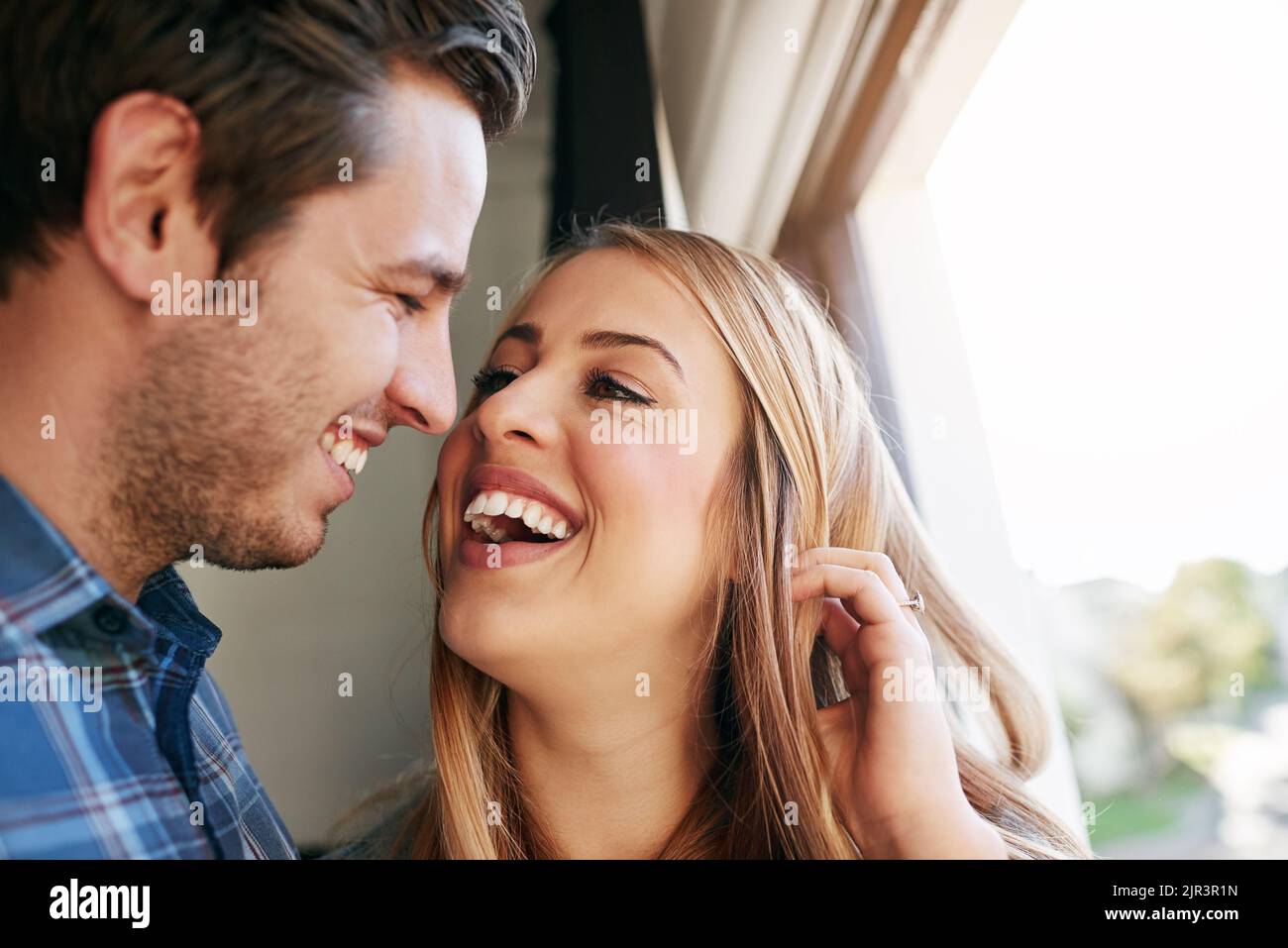 Lachen ist ein großer Teil ihrer Beziehung. Ein liebevolles junges Paar, das an einem Fenster in ihrem Haus steht. Stockfoto