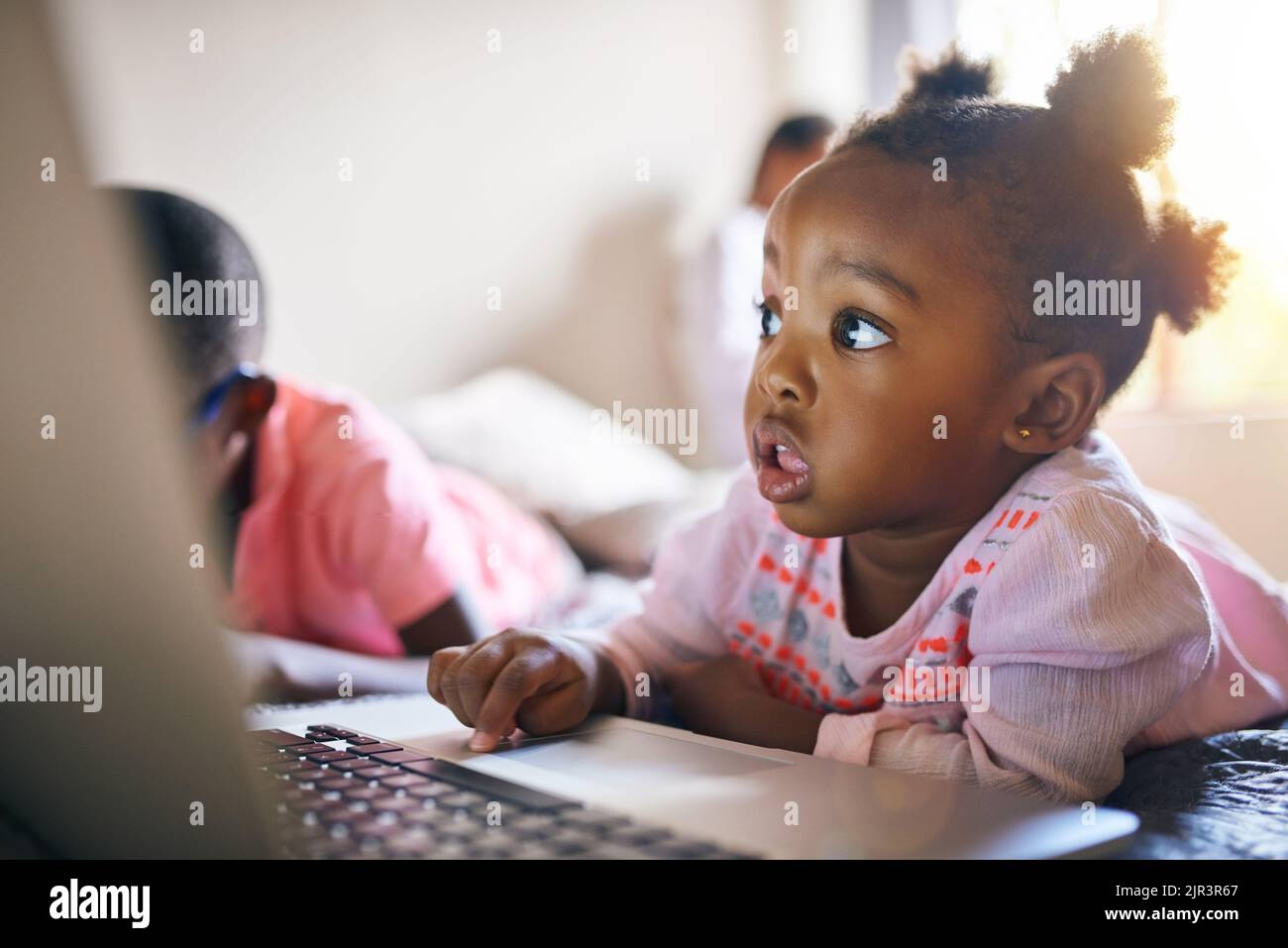 Das Internet ist ein wunderbarer Ort. Ein entzückendes kleines Mädchen spielt auf einem Laptop neben ihrem Bruder zu Hause. Stockfoto