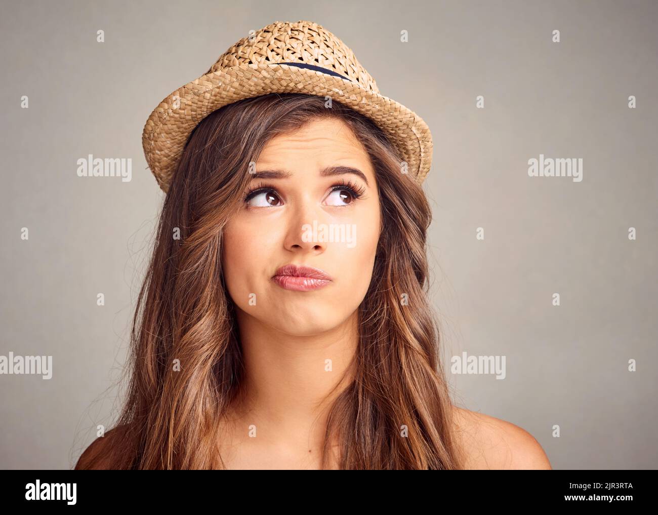 Hmmm... was zu tun ist. Studioaufnahme einer attraktiven jungen Frau, die vor grauem Hintergrund unsicher aussieht. Stockfoto