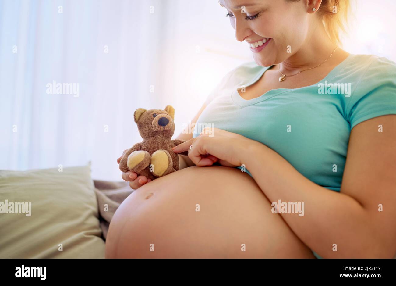 Nun haben Tonnen von Spaß, wenn das Baby kommt. Eine Schwangere mit einem Teddybär, während zu Hause entspannen. Stockfoto