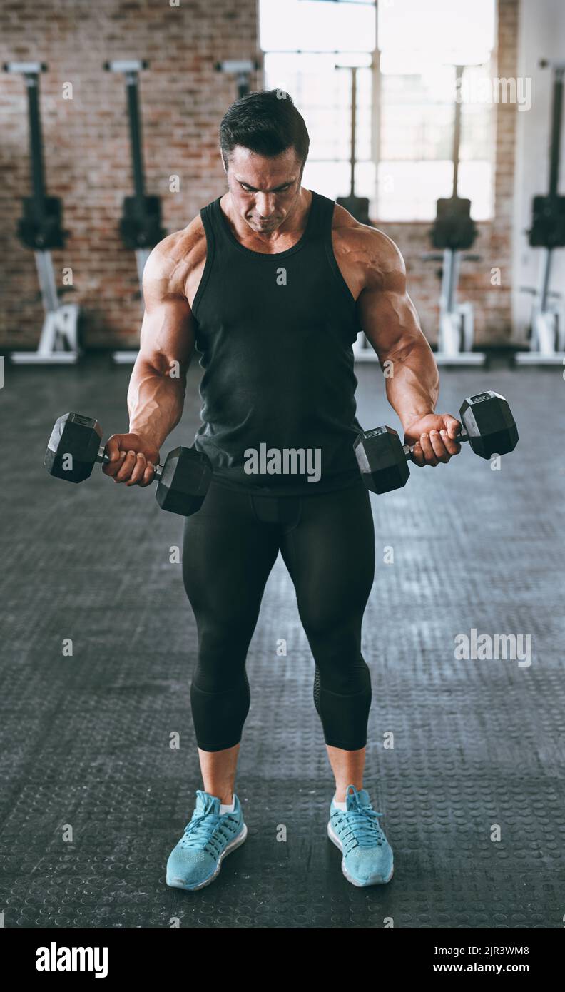 Ein junger Mann, der mit Hanteln im Fitnessstudio arbeitet. Stockfoto