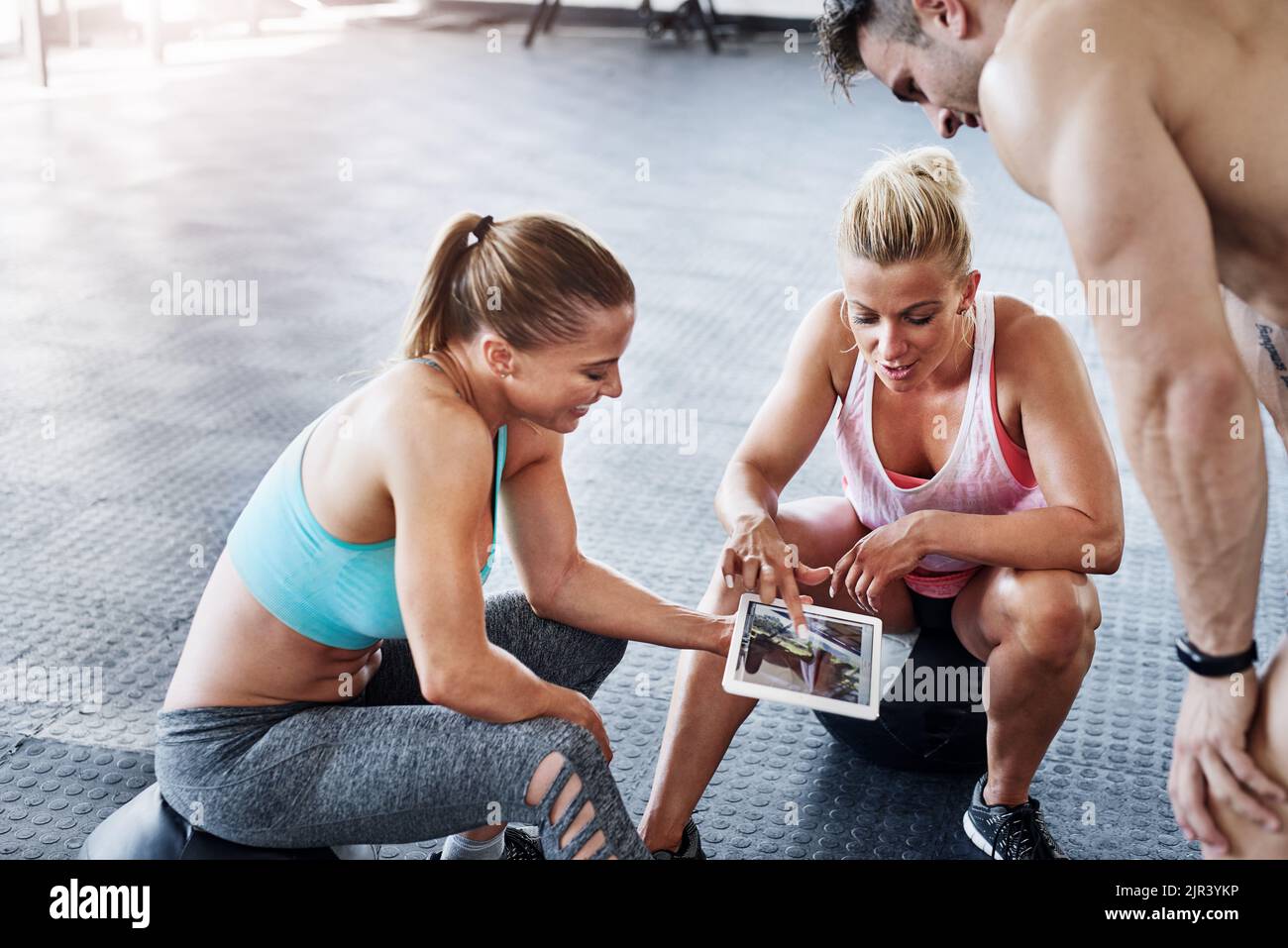 Es gibt eine Vielzahl von Fitness-Tutorials online. Eine Gruppe von Menschen mit einem digitalen Tablet im Fitnessstudio. Stockfoto