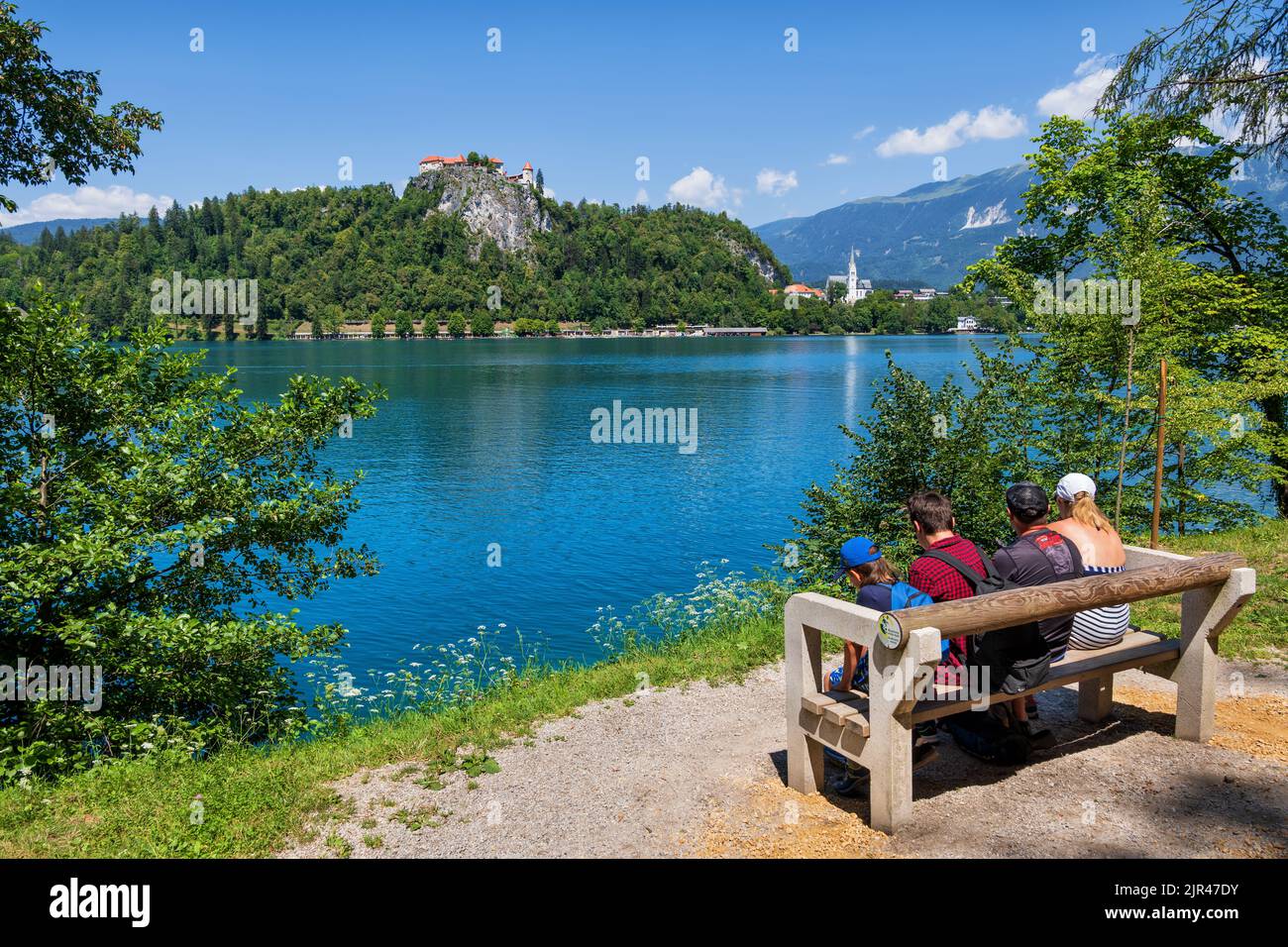 Bled, Slowenien - 18. Juli 2022: Die vierköpfige Familie genießt von einer Bank, einem beliebten Touristenziel, einen malerischen Blick auf den Bleder See und die Burg von Bled. Stockfoto
