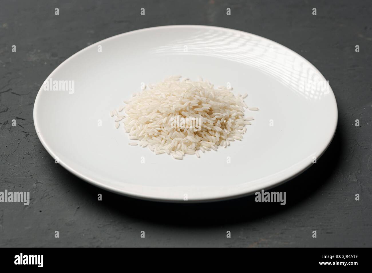 Haufen von trockenem Reis in einer Schüssel auf schwarzem Hintergrund, Mangel an Nahrung, Hunger-Konzept Stockfoto