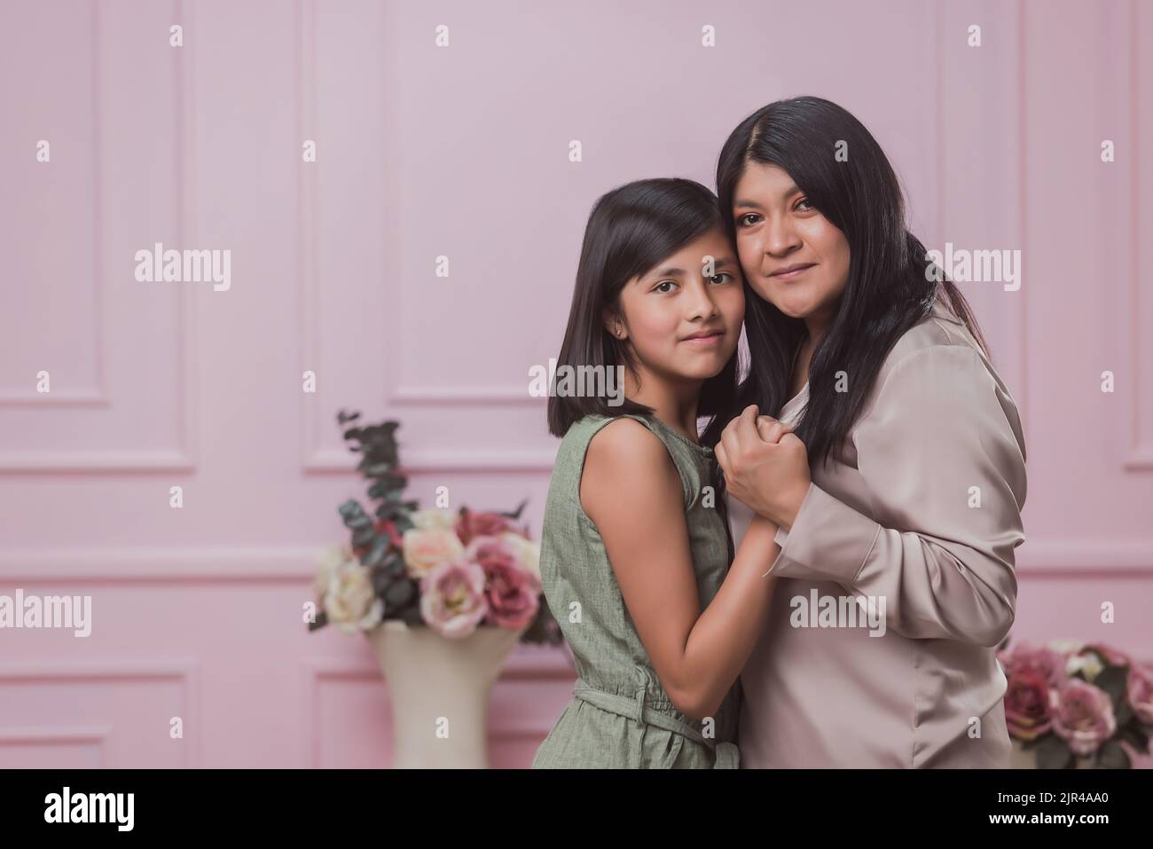 Eine hispanische Mutter mit ihrer Tochter, die sich auf einem rosa Hintergrund umarmt Stockfoto Eine hispanische Mutter mit ihrer Tochter, die sich auf einem rosa Hintergrund umarmt Stockfoto
