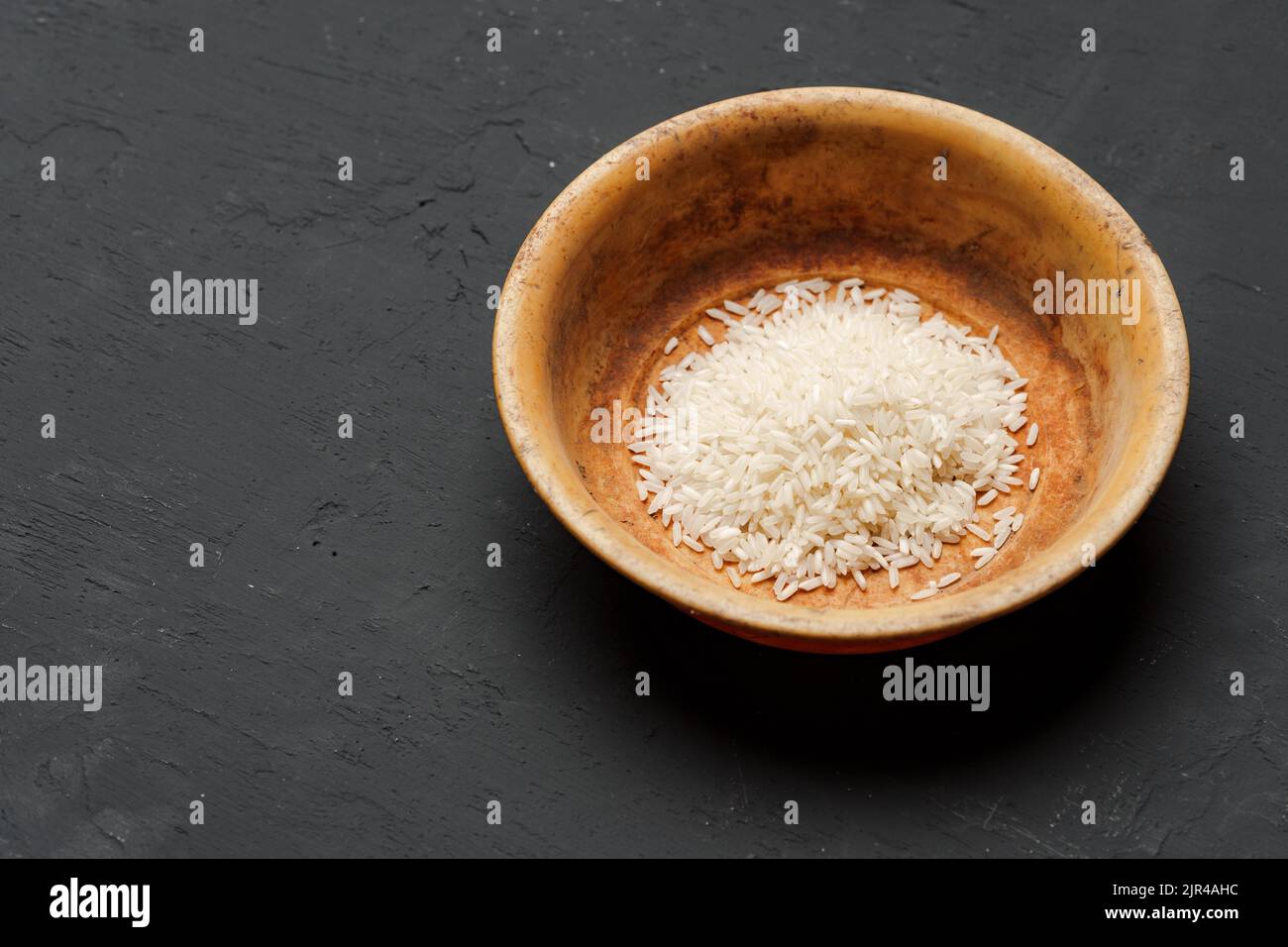 Haufen von trockenem Reis in einer Schüssel auf schwarzem Hintergrund, Mangel an Nahrung, Hunger-Konzept Stockfoto