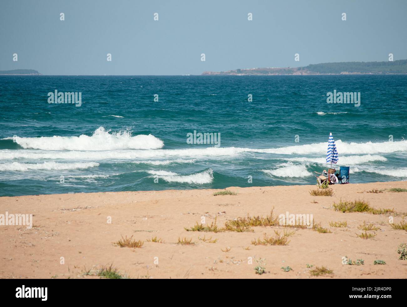 Sonnenschirm und zwei Campingliegen an einem einsamen Strand. Das Wellenmeer spült an Land. Entspannungsbereich abseits der Menschen. Sommer vibes Idee Konzept. Stockfoto