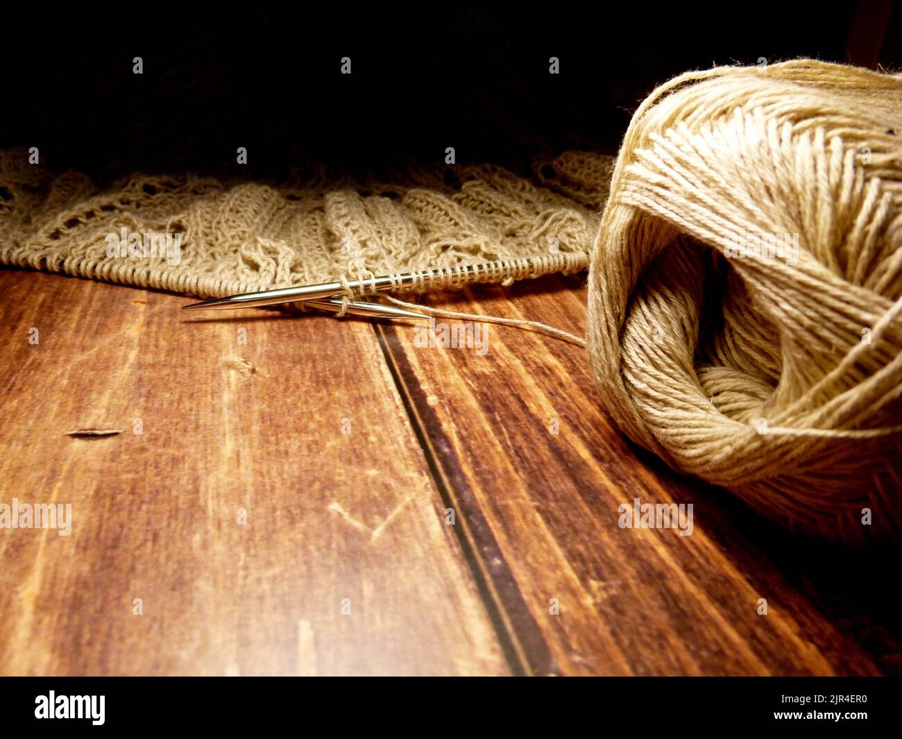 Durchbrochene Tischdecke beim Stricken. Stricknadeln, Schlaufen auf Stricknadeln, Strickstoff, Fadenknäuel, grobe Baumwolle und Leinen Stockfoto