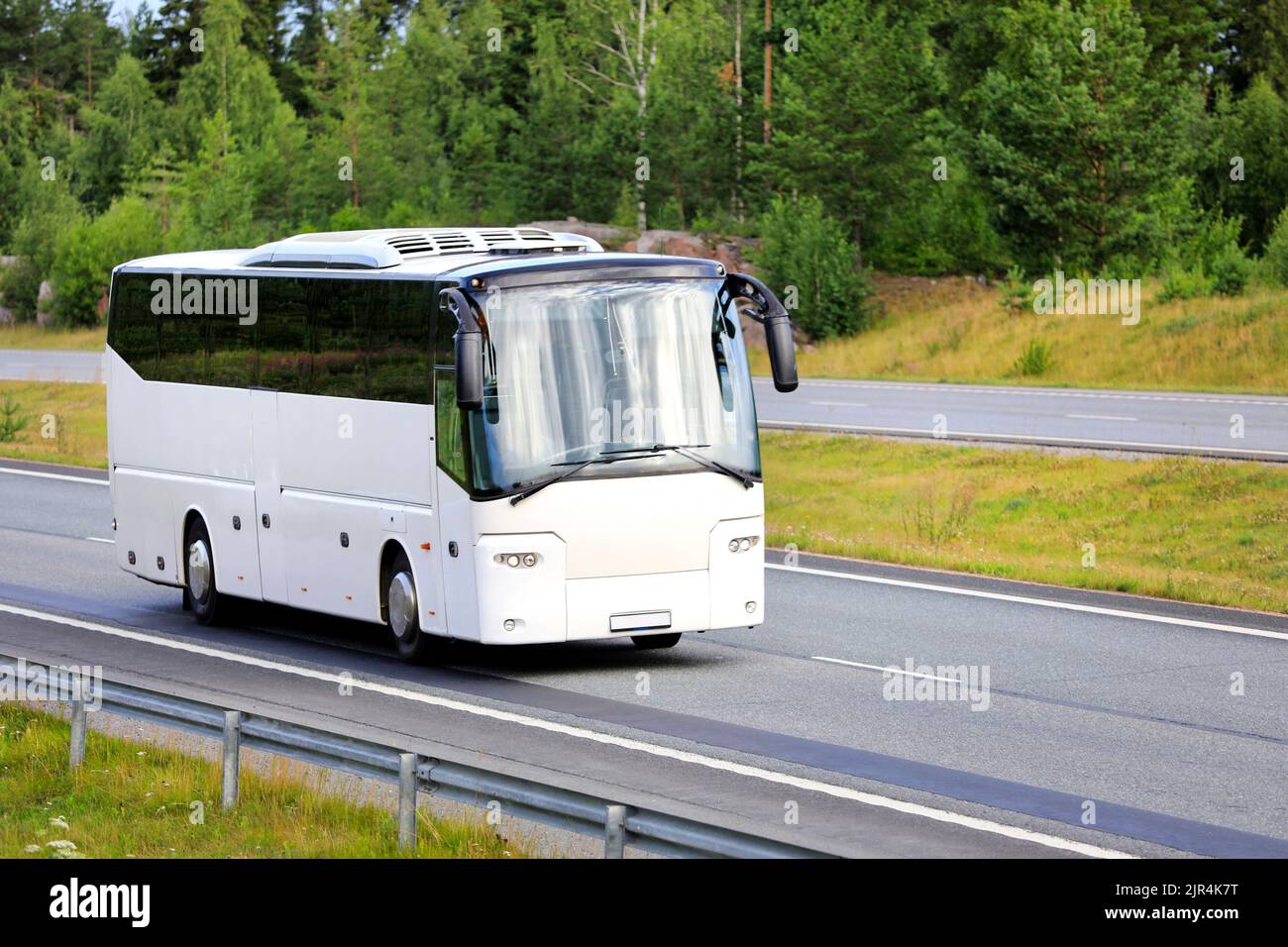 Weißer Reisebus, der an einem Sommertag mit hoher Geschwindigkeit auf der Autobahn fährt. Keine Personen, kopieren Sie Speicherplatz rechts vom Bild. Stockfoto