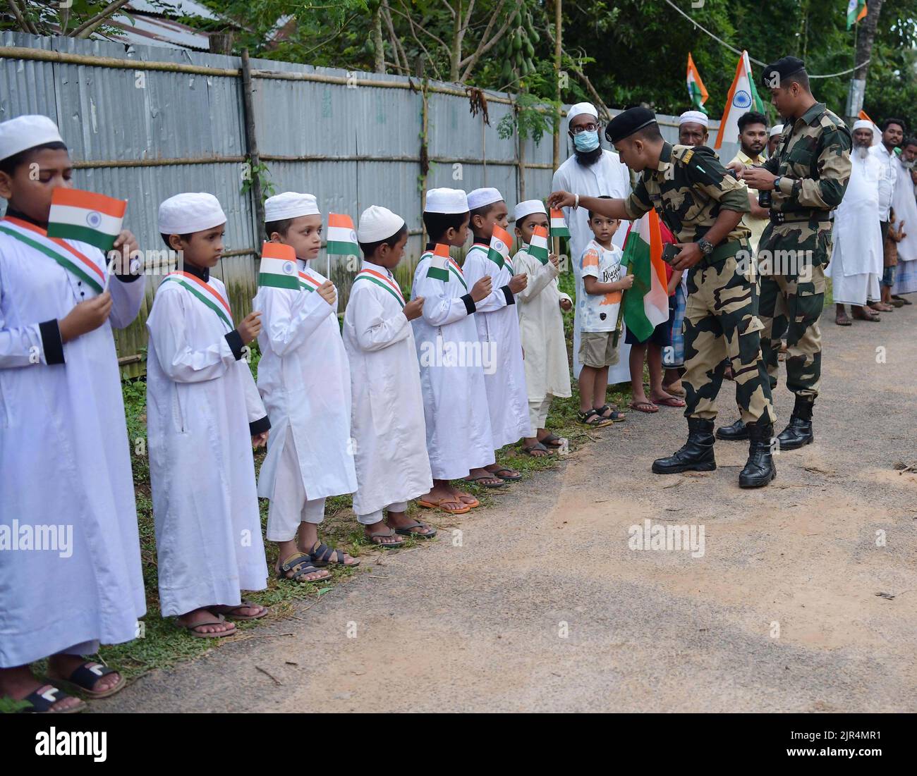 Beamte der BSF (Border Security Force) verteilen indische Flaggen an Kinder, um an einer „Tiranga Yatra“ teilzunehmen, die von der BSF (Border Security Force) im Rahmen der „Azadi ka Amrit Mahotsav“-Feierlichkeiten zum Gedenken an den 75.. Jahrestag des indischen Unabhängigkeitstages entlang der Grenze zwischen Indien und Bangladesch im Gebiet Boxanagar organisiert wird. Agartala. Tripura, Indien. Stockfoto