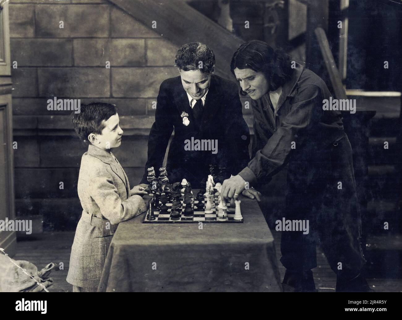 Douglas Fairbanks spielt Schach mit Samuel Reshevsky und Charlie Chaplin sieht sich das Spiel an, am Set des amerikanischen Stummfilms von Fairbanks die drei Musketiere. 1921. Stockfoto