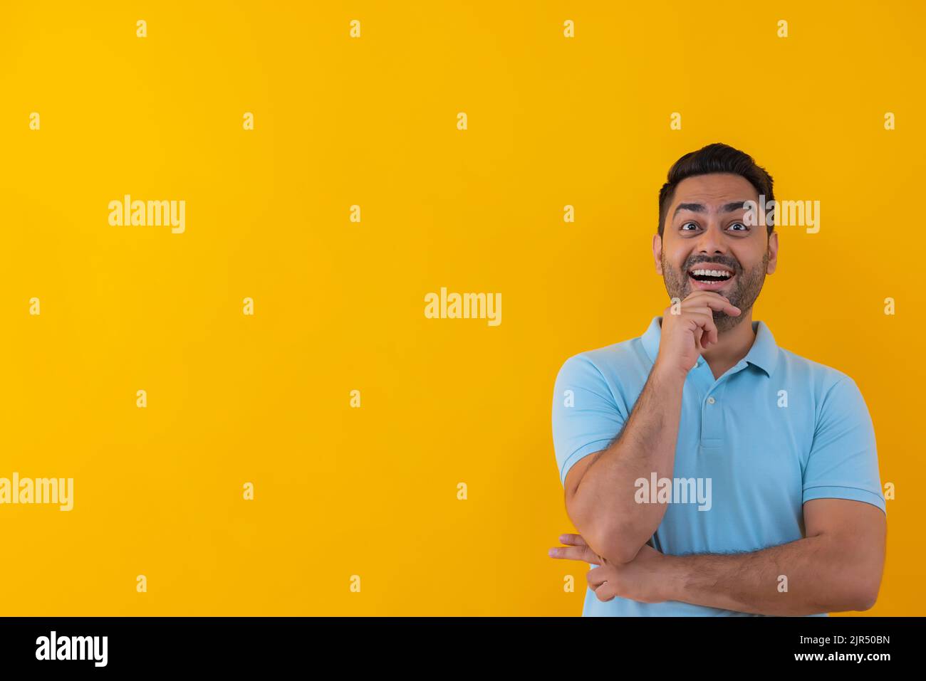 Porträt eines fröhlichen jungen Mannes, der auf einem gelben Hintergrund mit der Hand auf dem Kinn einen anderen Blick hat Stockfoto