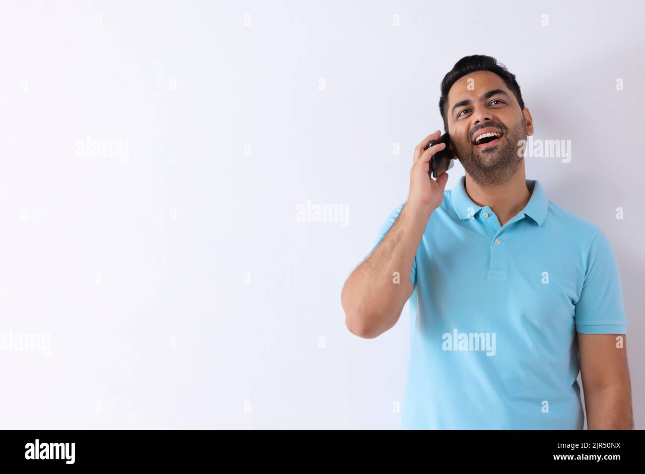 Fröhlicher junger Mann, der auf dem Smartphone spricht, während er vor weißem Hintergrund steht Stockfoto