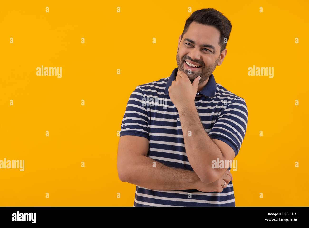Glücklicher junger Mann, der mit der Hand auf dem Kinn wegschaut Stockfoto
