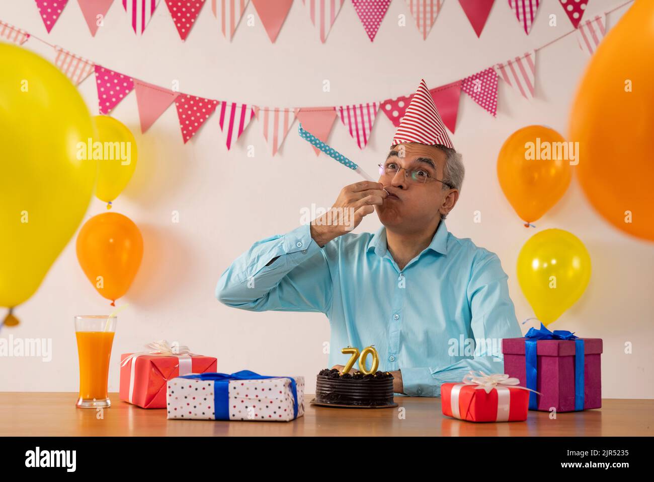 Glücklicher älterer Mann, der an seinem 70.. Geburtstag Party-Horn bläst Stockfoto
