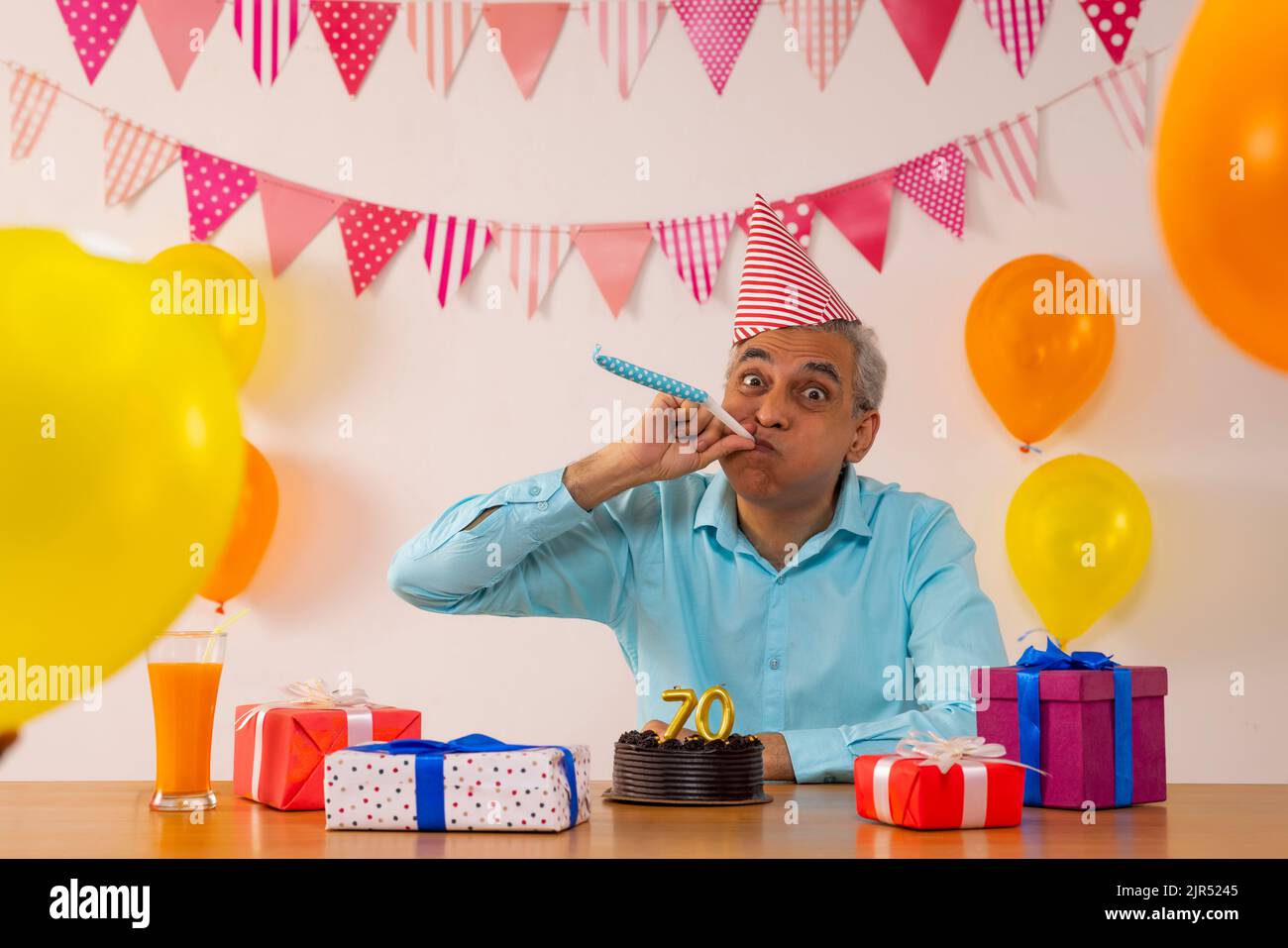 Glücklicher älterer Mann, der an seinem 70.. Geburtstag Party-Horn bläst Stockfoto
