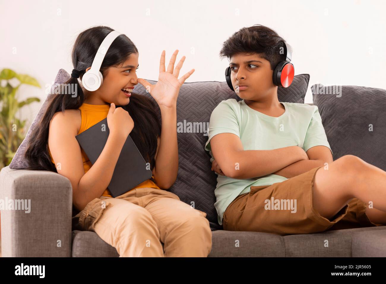 Die junge Schwester neckt ihren Bruder, während sie auf dem Sofa mit digitalem Tisch im Wohnzimmer sitzt Stockfoto