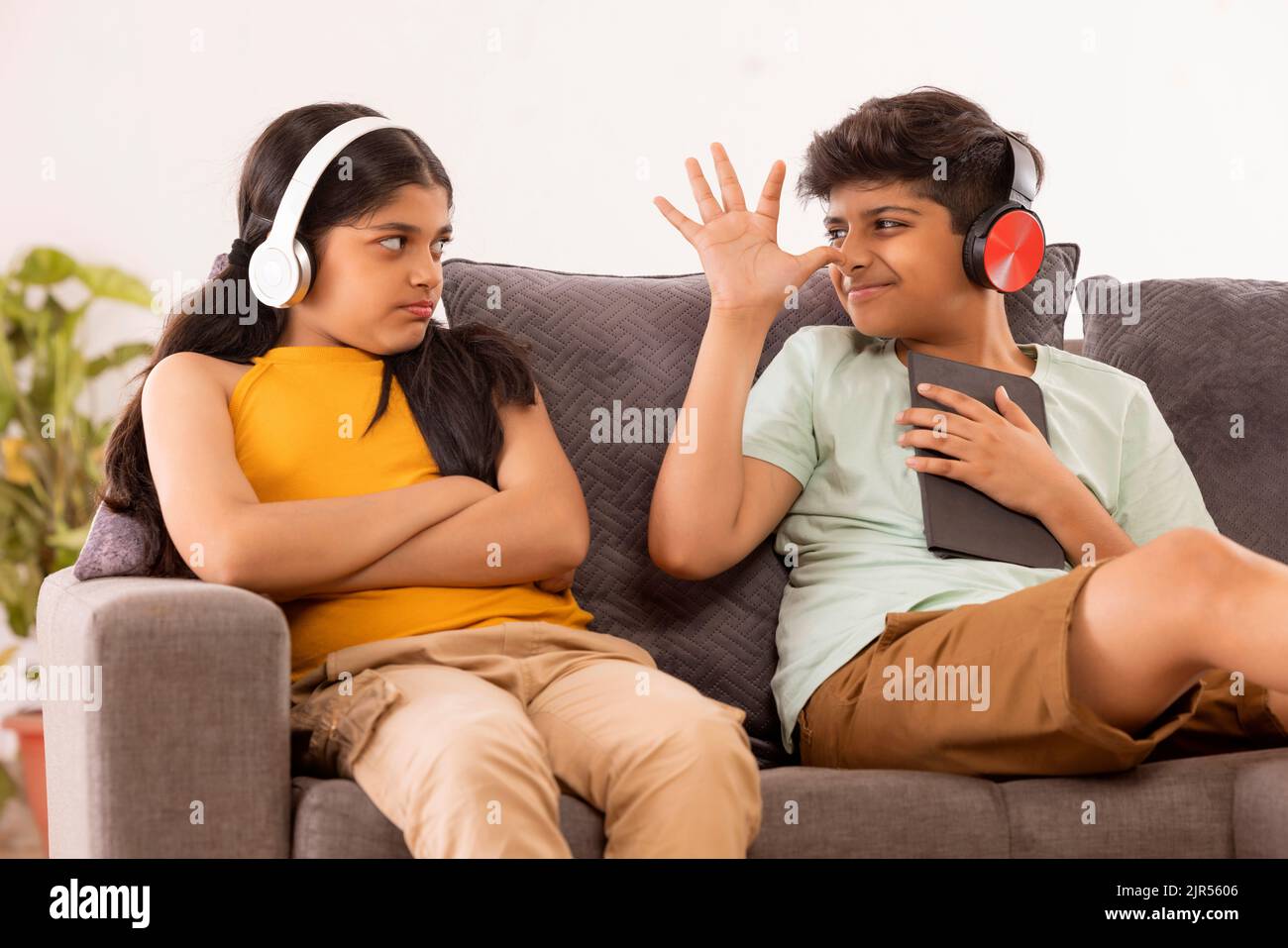 Der junge Bruder neckt seine Schwester, während er auf dem Sofa mit digitalem Tisch im Wohnzimmer sitzt Stockfoto