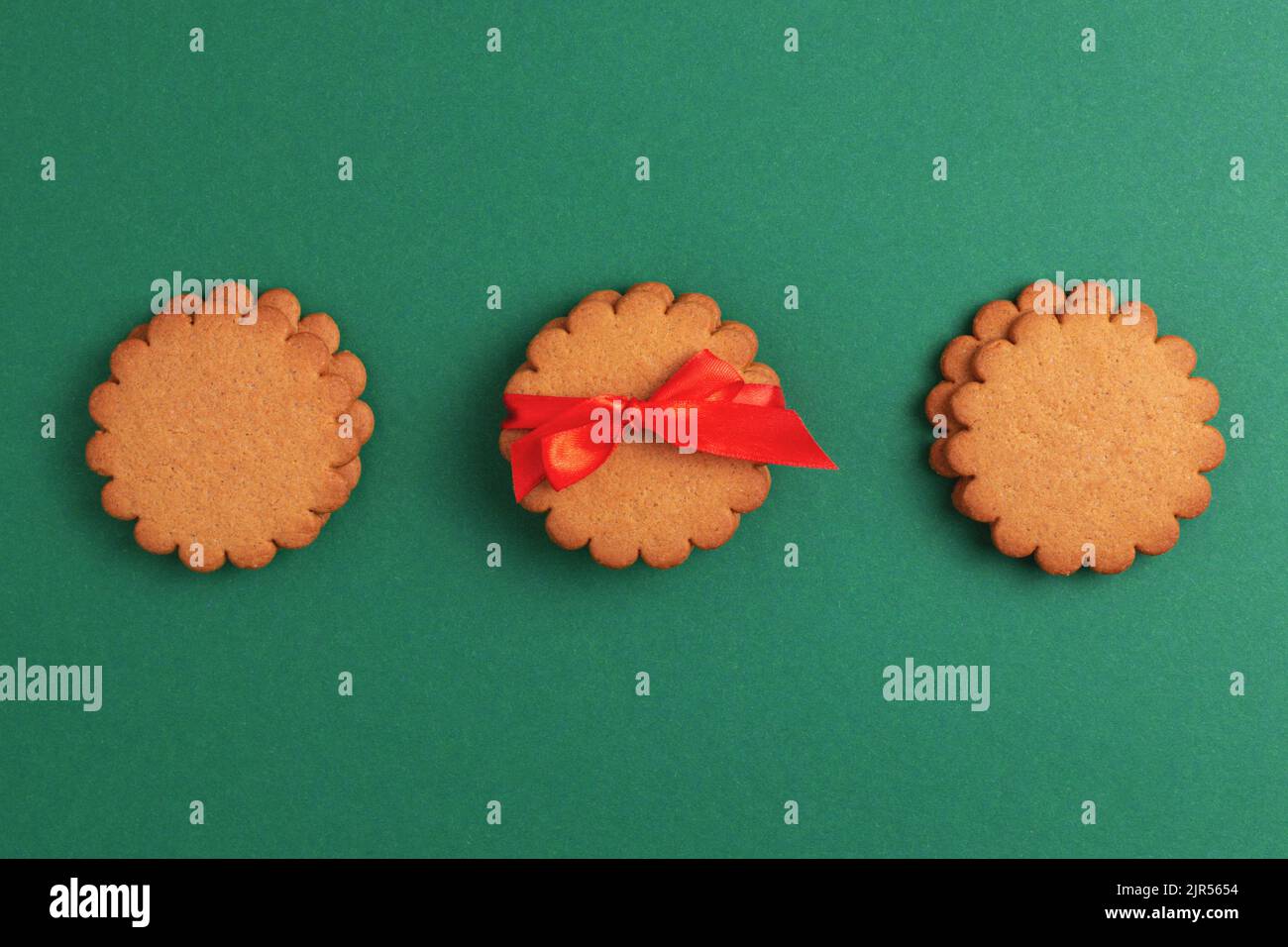 Lebkuchenkekse mit rotem Band auf grünem Hintergrund dekoriert. Traditionelle Weihnachtsgeschenke, Blick von oben. Stockfoto