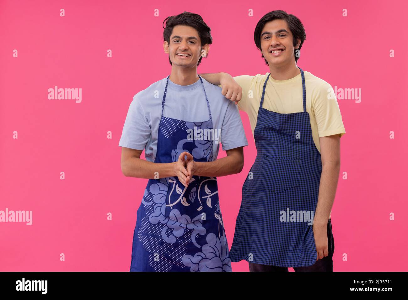 Zwei Jungen im Teenageralter auf der Kochschürze stehen zusammen vor rosa Hintergrund Stockfoto