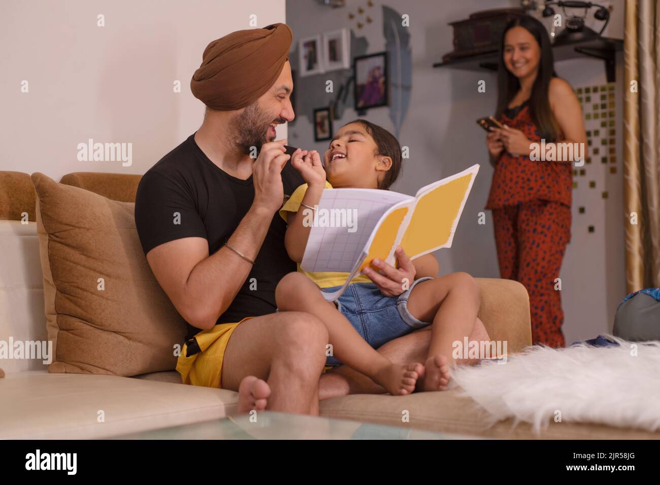 Vater hilft seiner Tochter bei den Hausaufgaben, während die Mutter wegsteht Stockfoto