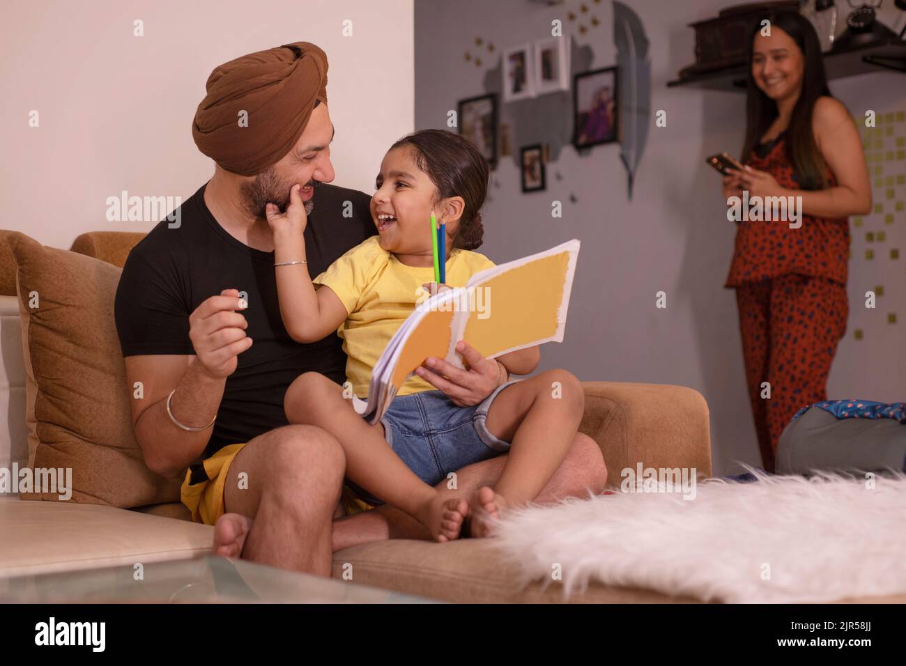 Vater hilft seiner Tochter bei den Hausaufgaben, während die Mutter wegsteht Stockfoto