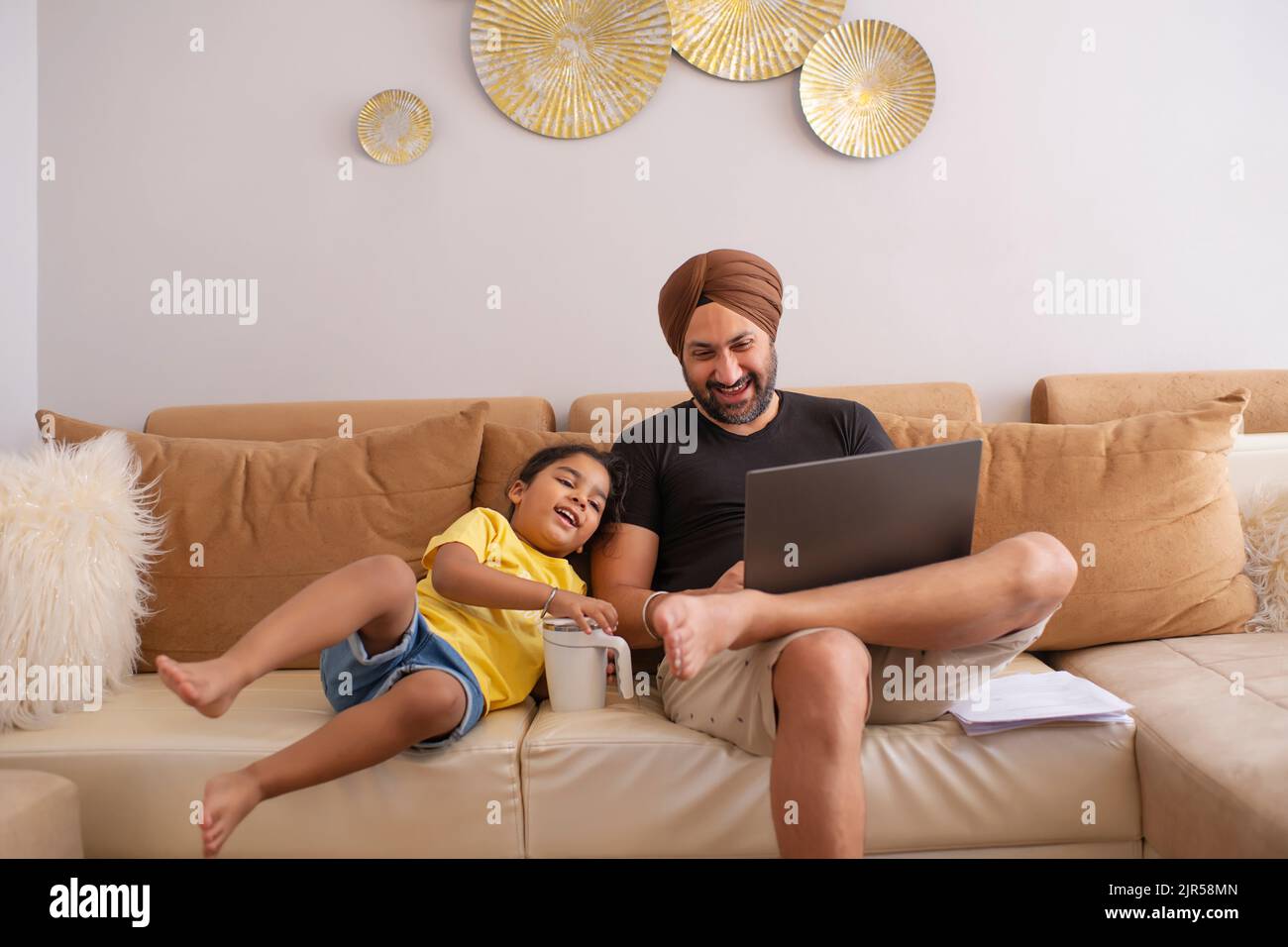 Vater und Tochter schauen sich im Wohnzimmer Cartoons auf dem Laptop an Stockfoto