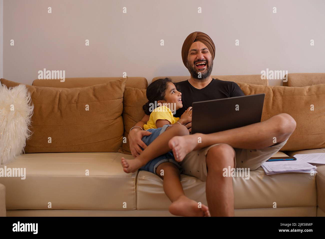 Vater und Tochter schauen sich im Wohnzimmer Cartoons auf dem Laptop an Stockfoto