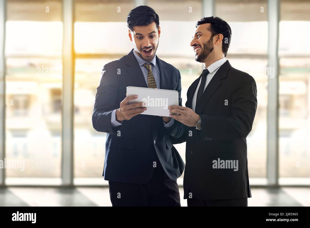 Firmenmitarbeiter in formellen Geschäftskleidung schauen sich ein digitales Tablet an, reden und lachen. Stockfoto