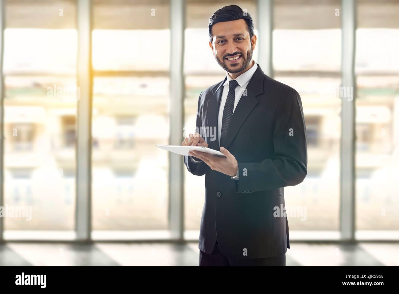 Ein Unternehmensangestellter, der in einem formellen Geschäftsanzug ein digitales Tablet in seinem Büro hält. Stockfoto