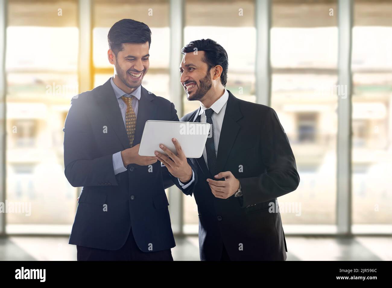 Firmenmitarbeiter in formellen Geschäftskleidung schauen sich ein digitales Tablet an, reden und lachen. Stockfoto