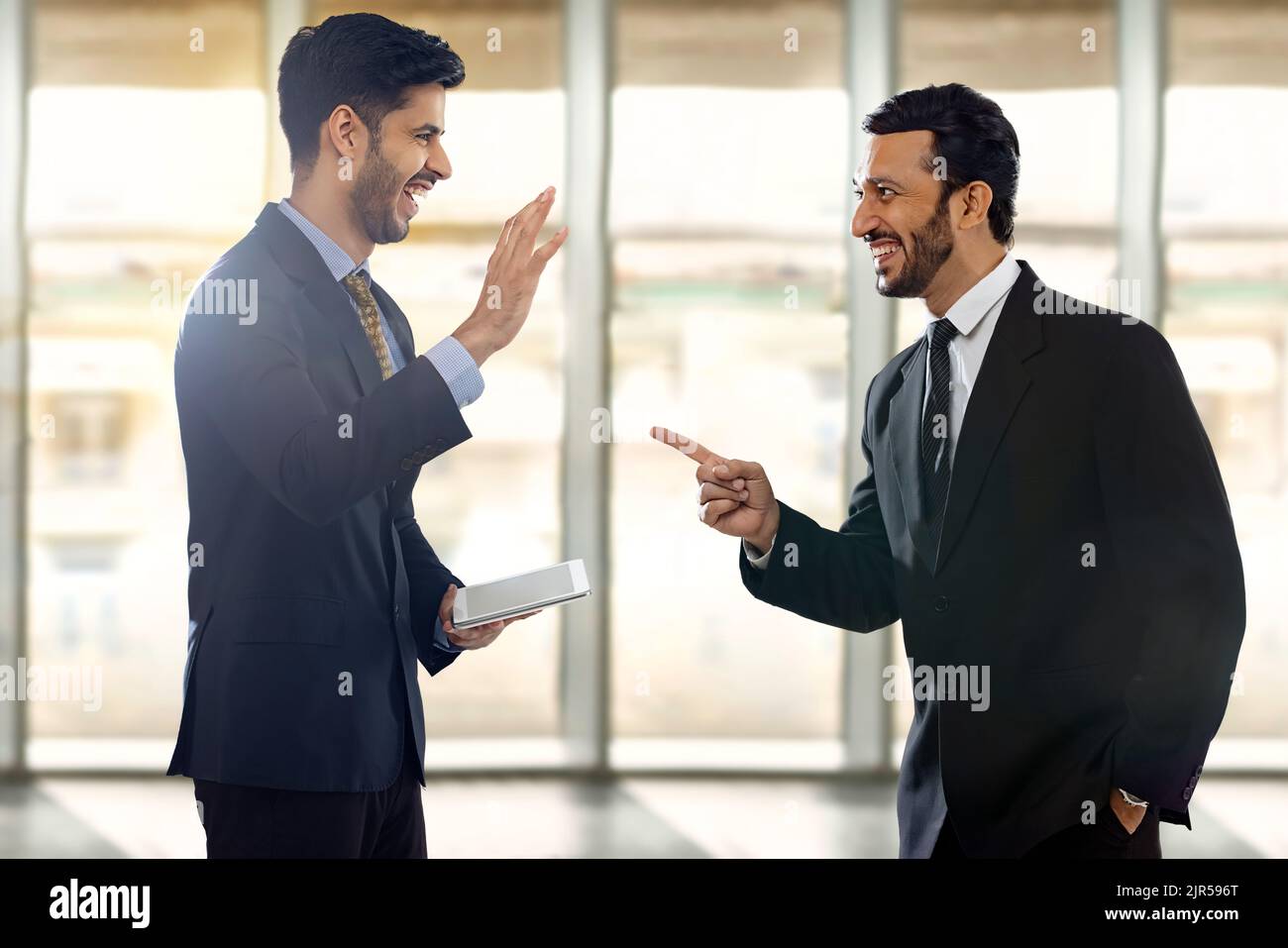 Unternehmensmitarbeiter in formellen Geschäftskleidung reden und lachen mit einem von ihnen, der die digitale Registerkarte hält. Stockfoto