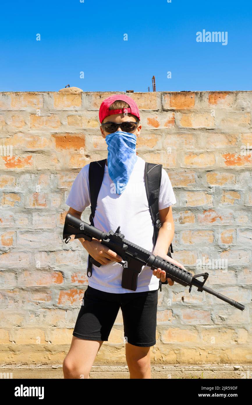 Bewaffneter Junge mit einem Gewehr, das Bandana und eine Mütze trägt Stockfoto