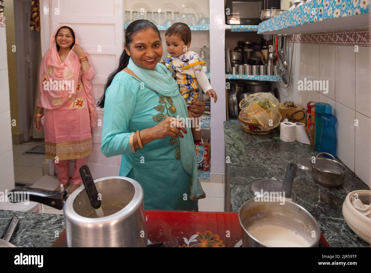 Porträt einer älteren Frau mit einem Enkelkind in der Küche und einer Schwiegertochter, die wegsteht Stockfoto