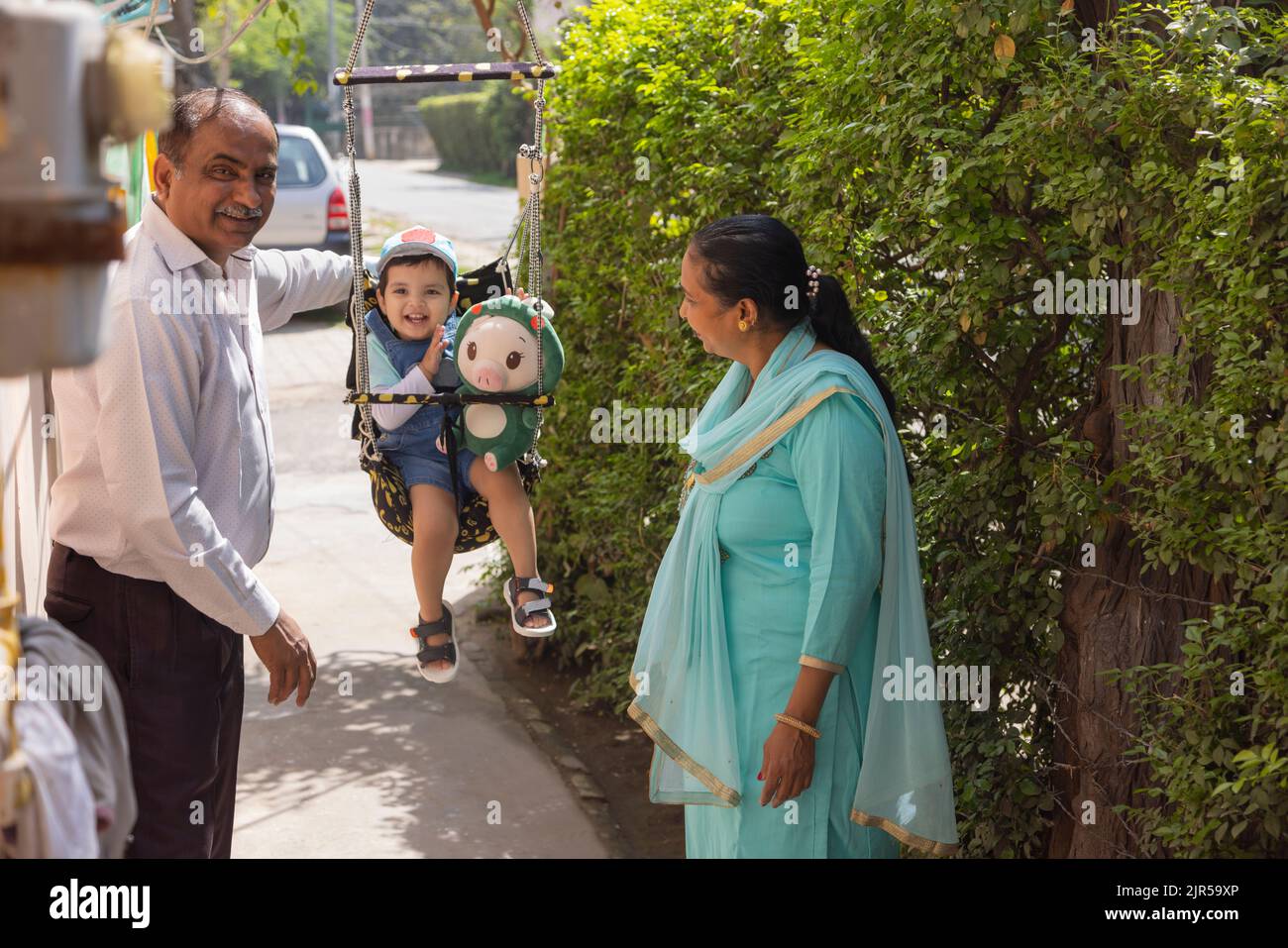 Großeltern haben Spaß mit Enkelkind auf Schaukel sitzen Stockfoto